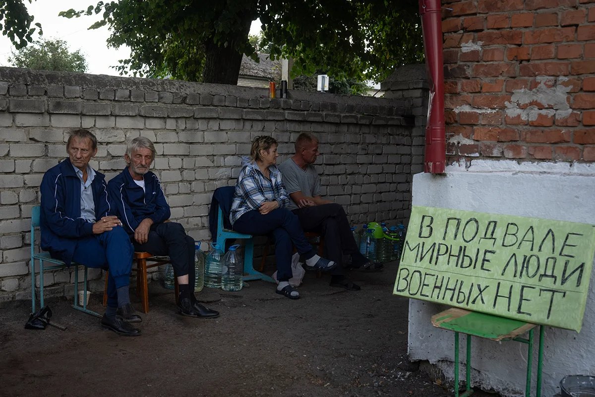 Locals sit outside a bomb shelter in Sudzha, with a sign reading “Civilians in the basement. There are no servicemen.” Photo: AP / Scanpix / LETA