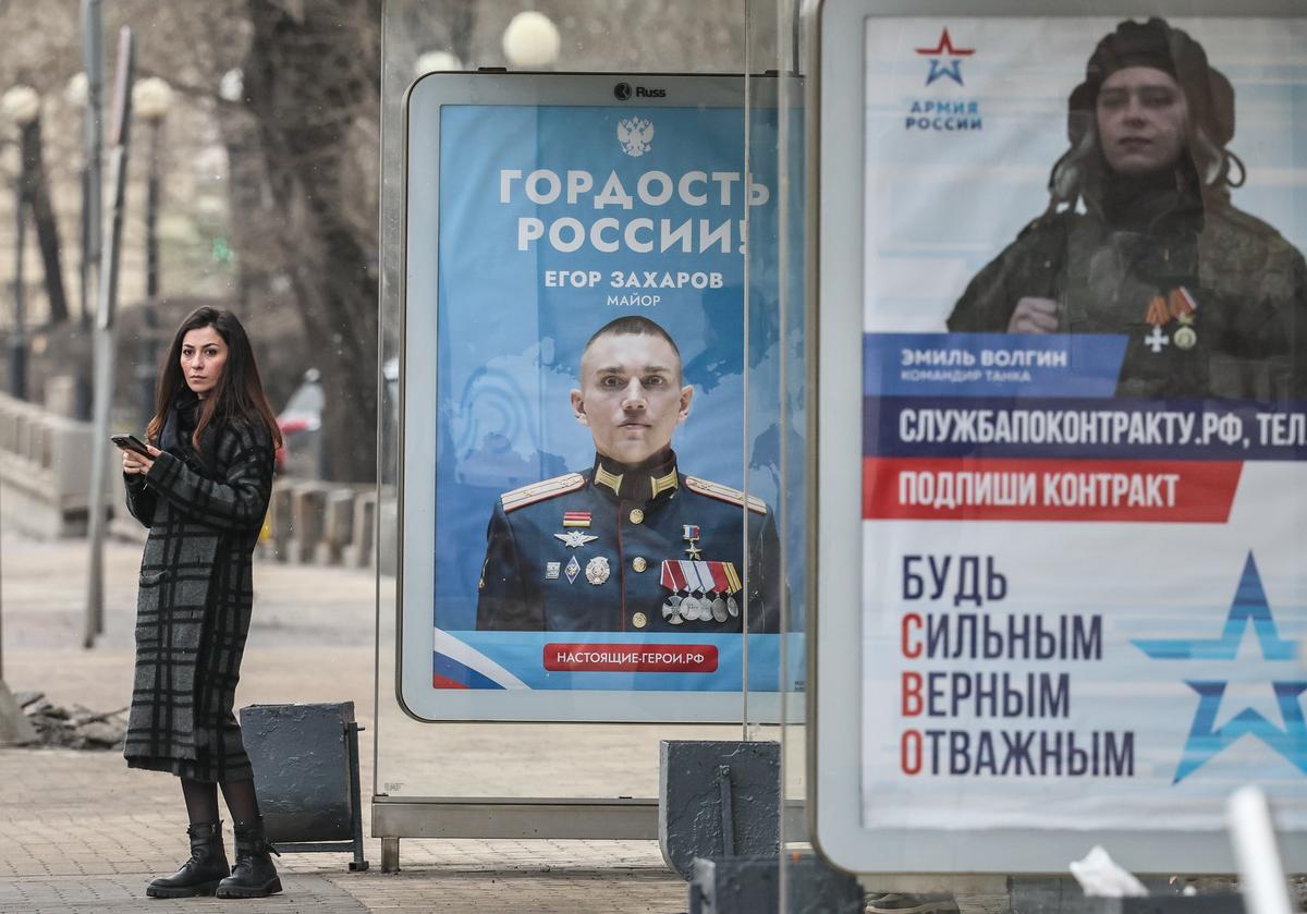 A woman waits at a bus stop with military conscription adverts in Moscow, Russia, 19 March 2025. Photo: EPA/YURI KOCHETKOV
